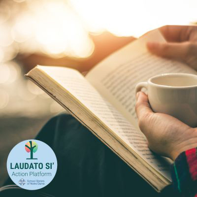 Stock photo image of a person reading a book while holding a cup of coffee, including SSND Laudato Si circle graphic on the bottom corner