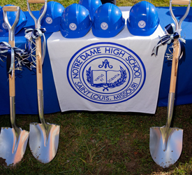 Photo of shovels with blue and white bows and hardhats sitting on a table with the Notre Dame High School logo in preparation for the groundbreaking ceremony