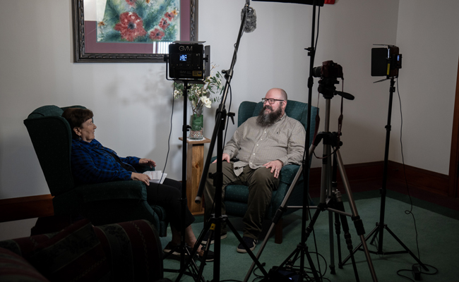 Adam Schicker and Sister Jan, surrounded by recording and photography equipment, prepare to record a new installment of the Called to Action podcast